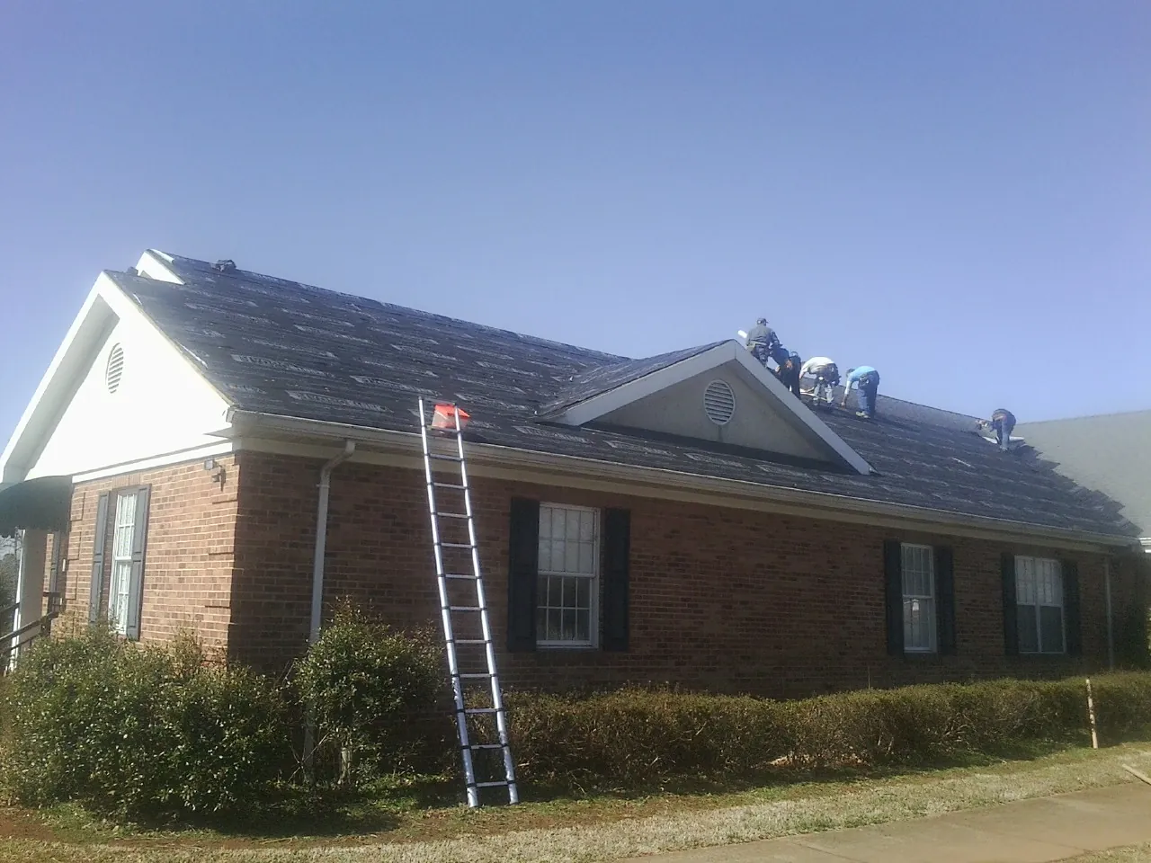 Crew tearing shingles off a brick ranch roof with a ladder set — Metal Roof Repair work by our crew in Marshfield