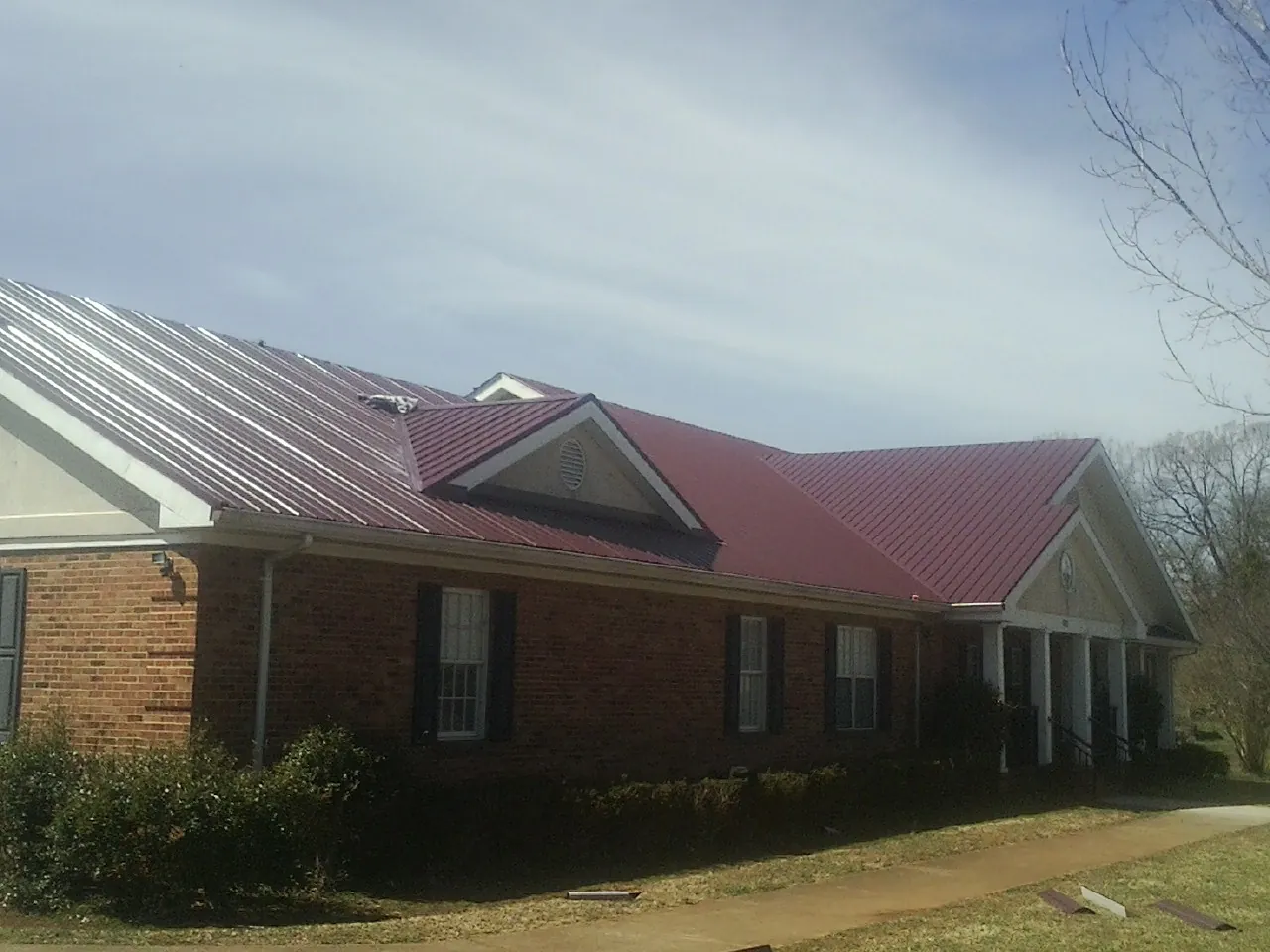 Red metal roof with gabled entries on a long brick building, from a Hail Damage Roof Repair job in Marshfield