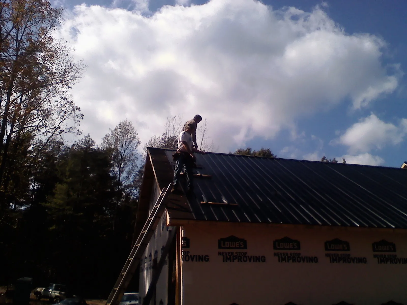 Roofer fastening dark metal panels high against a cloudy sky, from a Roof Inspection job in Marshfield