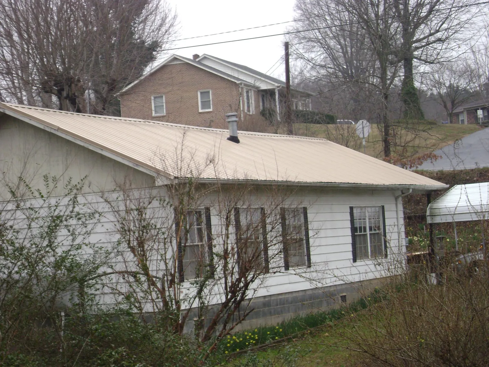 Tan metal roof on a white sided house set into a hillside — Commercial Roofing by Roofing Brothers in Marshfield